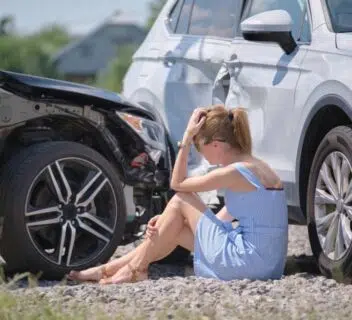 A woman sitting on the ground holding her head and leg after a car accident